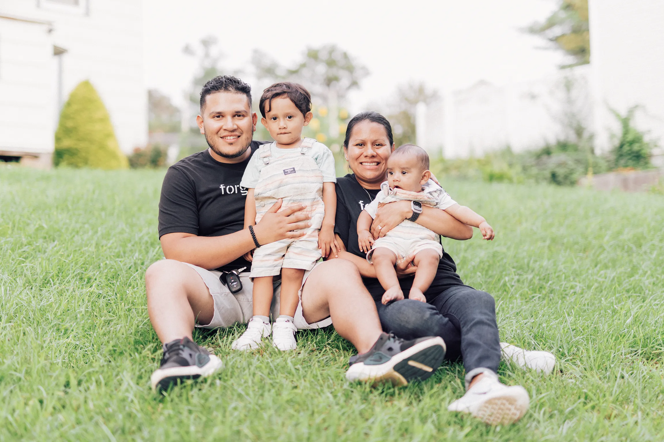 Outdoor family portrait taken in Brewster NY, featuring two parents sitting in the grass with their young children, smiling warmly during a natural light session.
