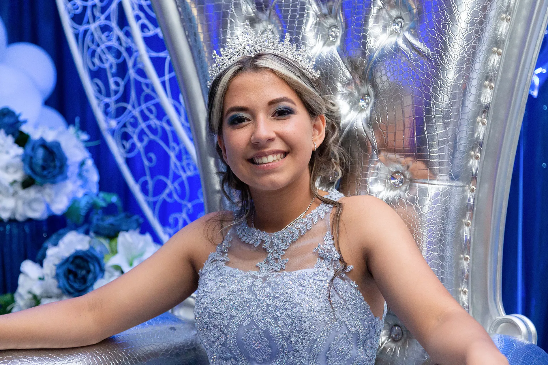 Indoor Quinceañera throne portrait — Fabiola sitting on an elegant silver chair wearing a light blue quince dress | Retrato de quinceañera en trono plateado con vestido azul claro.