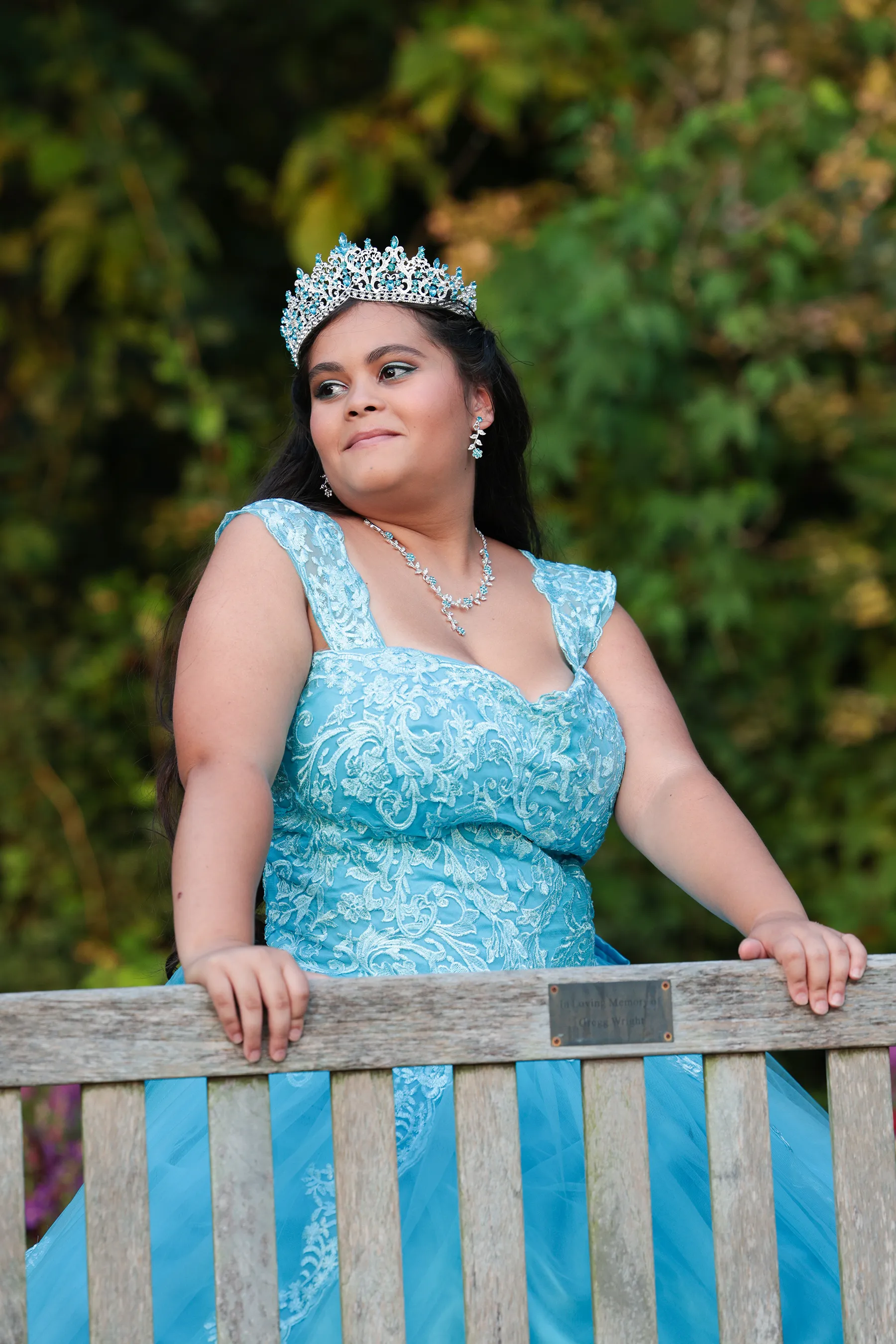 Quinceañera portrait sitting on a wooden bench at the Orange County Arboretum in Montgomery NY, wearing a sparkly blue vestido quince — elegant Sweet 15 photography with natural garden backdrop.